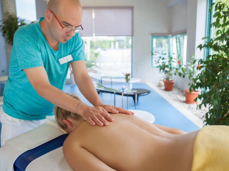 Un uomo fa un massaggio alla schiena a una persona sdraiata su un lettino da massaggio in una stanza luminosa.