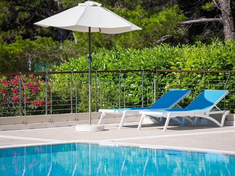 Due lettini blu accanto a una piscina con un ombrellone bianco e siepe verde sullo sfondo