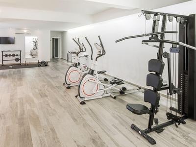 Palestra moderna in hotel con attrezzature cardio e pesi in una stanza luminosa.