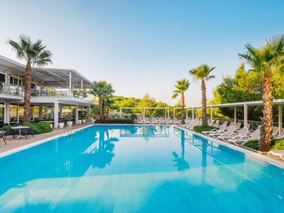 Piscina di un hotel moderno con lettini e palme sotto un cielo azzurro limpido