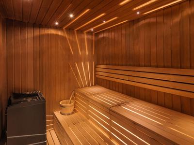 Světelná finská sauna s dřevěnými lavicemi, vědrem na nalévání a saunovou kamnou.