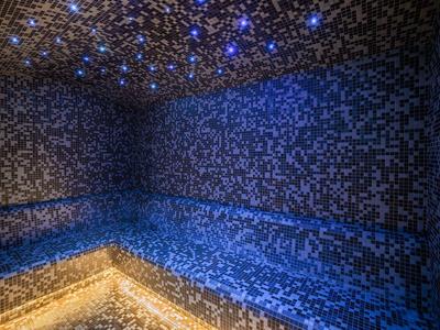Tmavá místnost v parní lázni s modro-černými mozaikovými stěnami a světelným efektem hvězdné oblohy