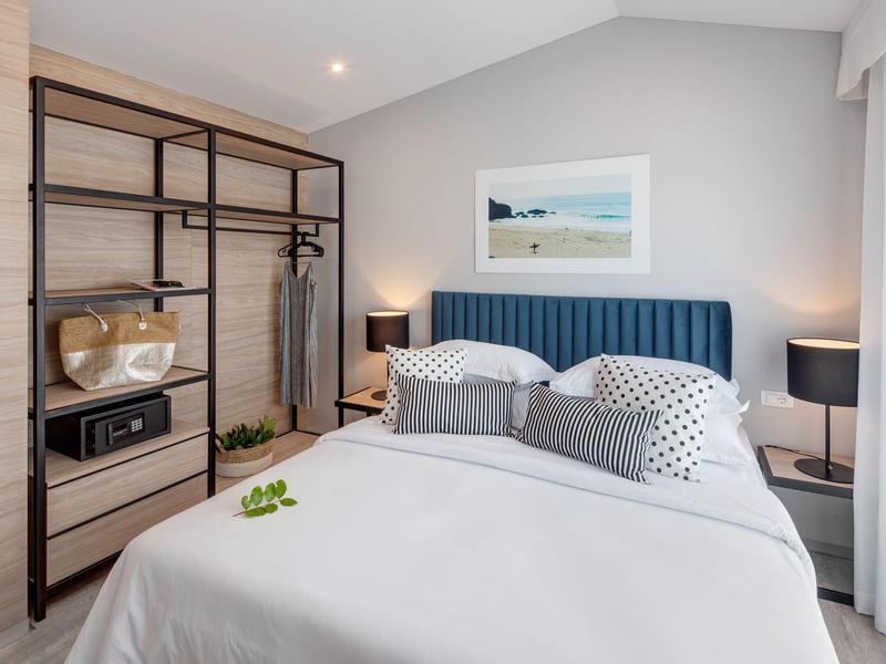 Moderně zařízená ložnice s velkou postelí, otevřenou šatní skříní a dvěma nočními stolky.