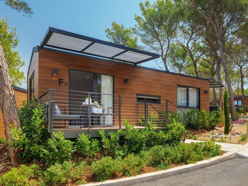 Moderní rekreační dům s dřevěným obkladem a terasou v lesnatém prostředí.