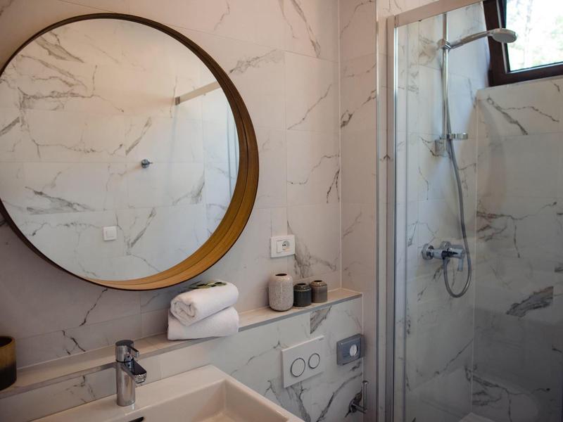 Moderní koupelnový prostor se kulatým zrcadlem, umyvadlem a sprchou se skleněnými dveřmi