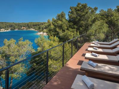 Terrazza con lettini e vista sul mare turchese e alberi verdi.