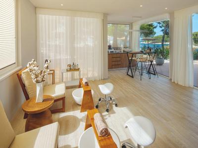 Salone spa luminoso con comode sedute, sgabelli bianchi e vista sulla terrazza esterna.