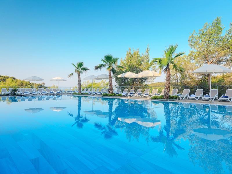 Piscina all'aperto con sdraio e ombrelloni sotto un cielo azzurro.