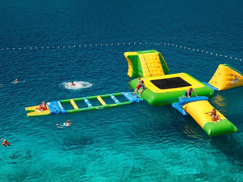 Percorso gonfiabile giallo e verde su mare blu con bagnanti intorno.