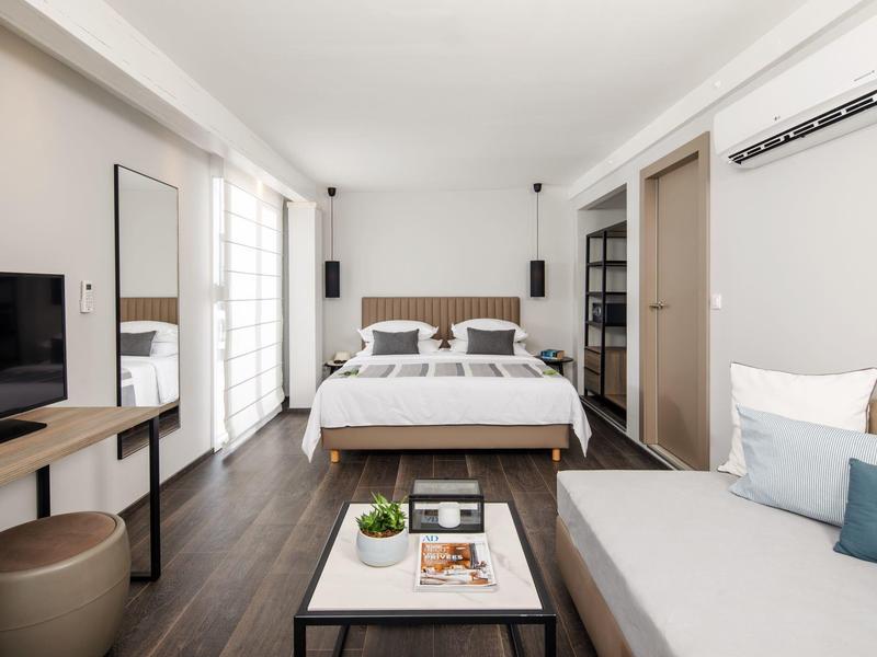 Camera moderna con letto matrimoniale, divano, TV e grande finestra luminosa.