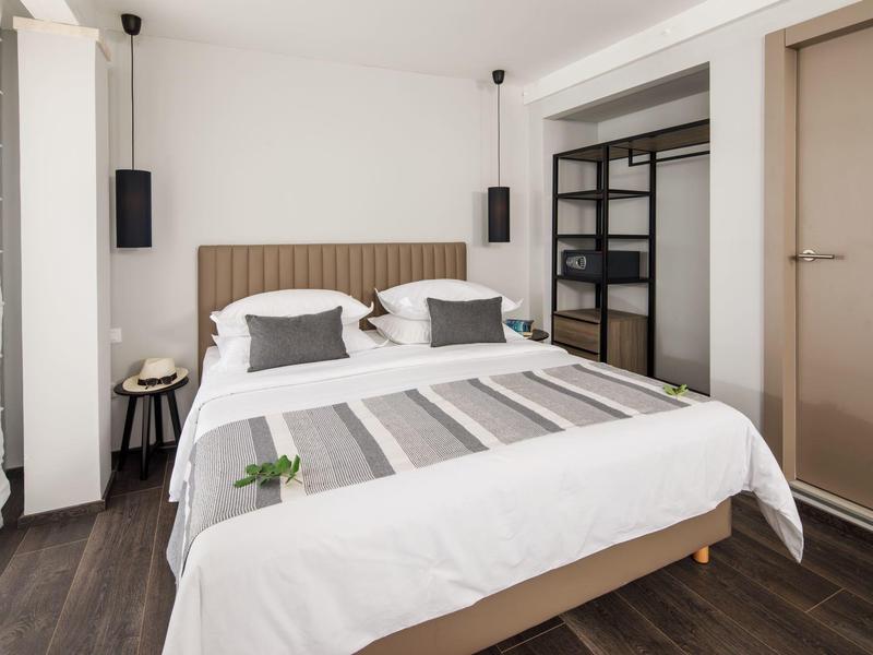 Camera d'hotel moderna con letto matrimoniale, arredo minimalista e pavimento scuro.