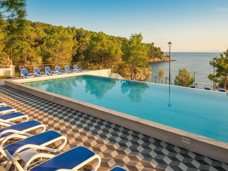 Piscina a sfioro con lettini blu, vista sul mare e sulla foresta.