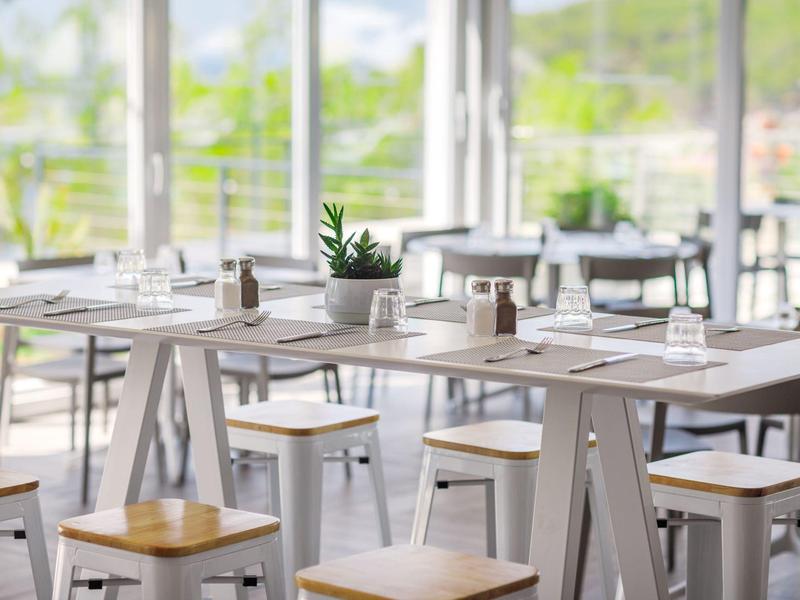 Sala da pranzo luminosa con tavoli in legno chiaro e sedie in un ambiente moderno.