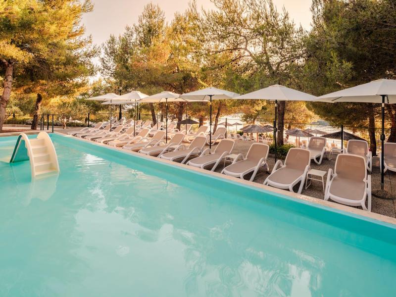 Piscina all'aperto con lettini e ombrelloni circondata da alberi.