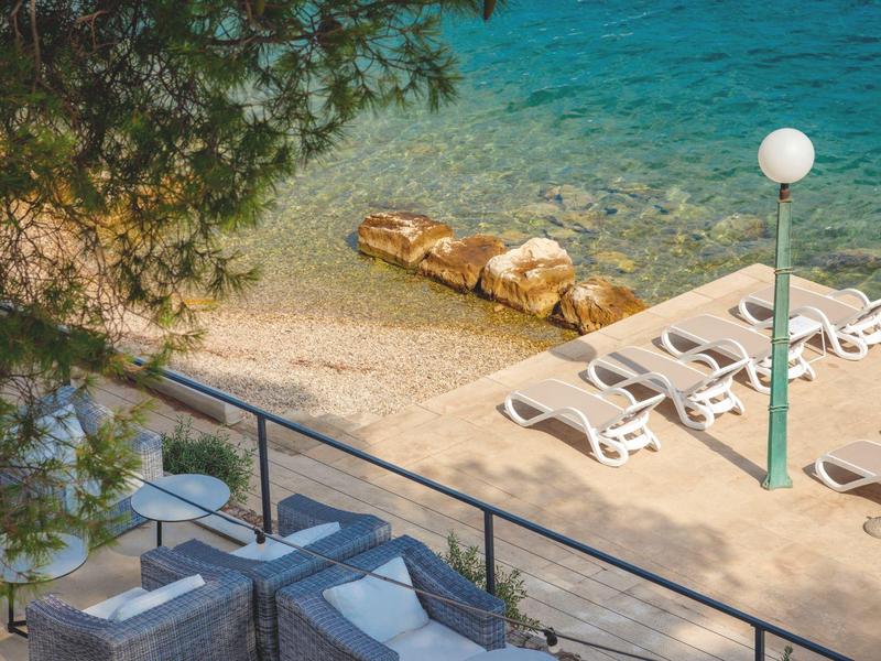 Strand mit weißen Liegestühlen und klarem blauem Wasser an einem sonnigen Tag.