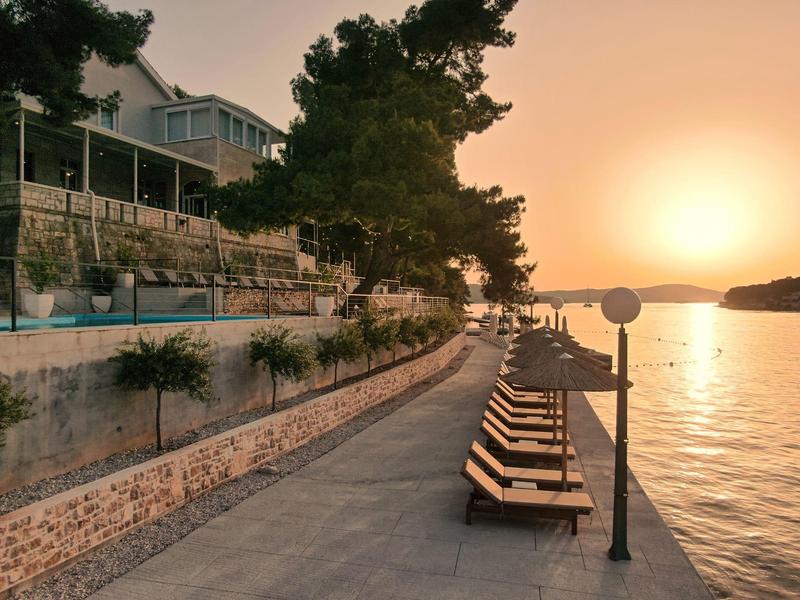 Leerer Weg mit Liegestühlen am Ufer bei Sonnenuntergang mit Blick auf das Wasser.