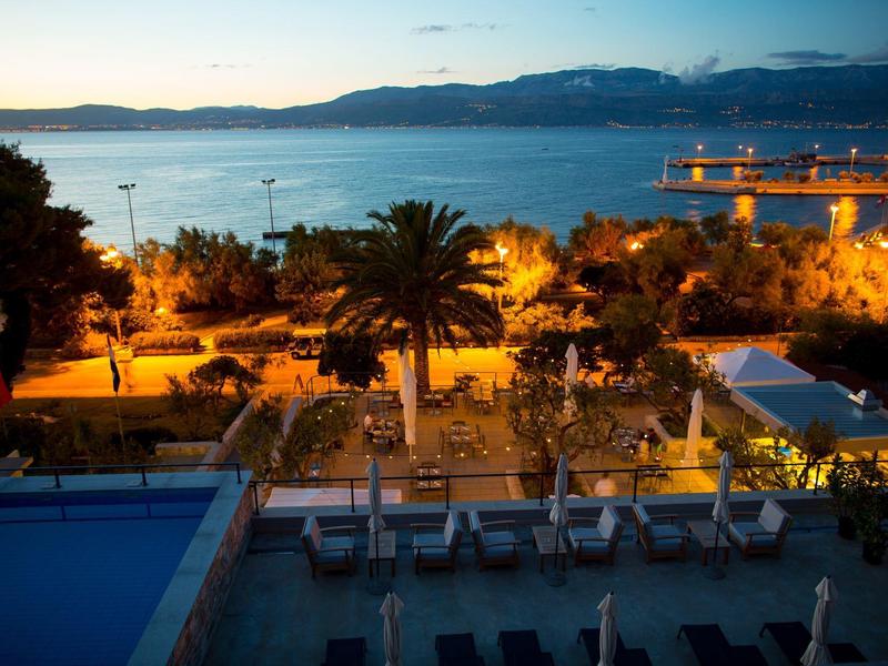 Avondelijke kustlandschap met zwembad, palmbomen en verlichte gebouwen aan zee.