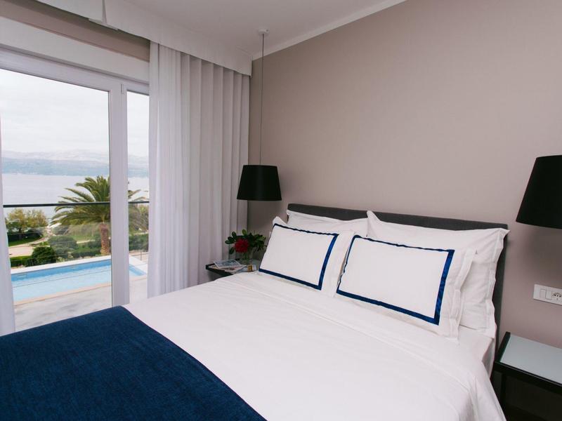 Moderne slaapkamer met groot bed, glasraam en uitzicht op een zwembad en de zee.