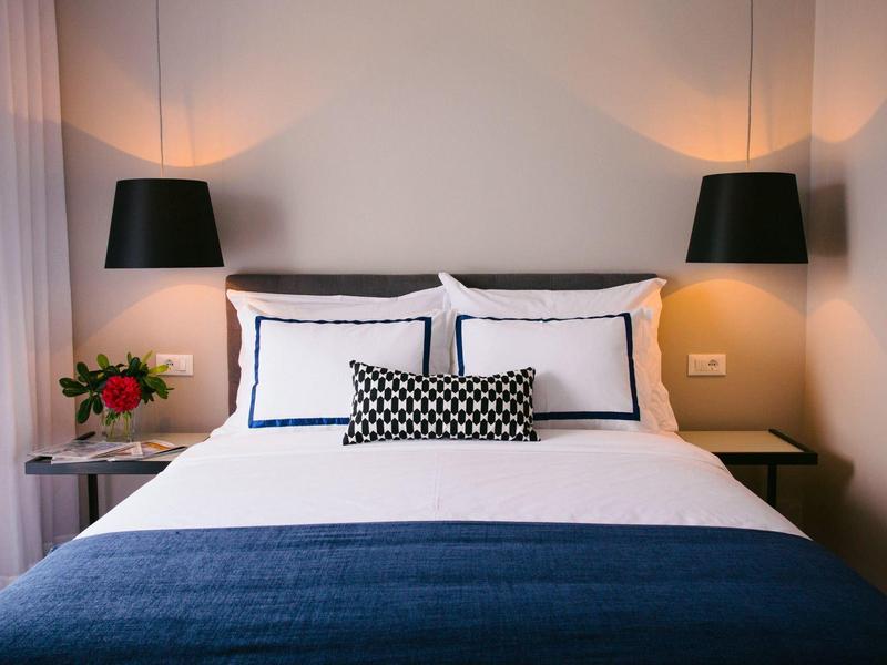 Modern hotelkamer met comfortabel bed, nachtkastjes en zwarte wandlampen.