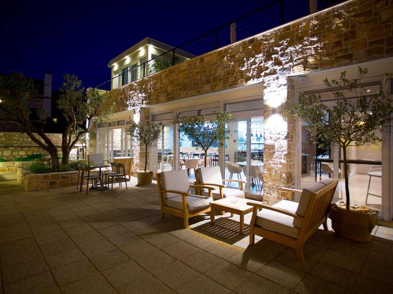 Verlichte terras met houten meubels naast een bakstenen muur in de nacht.