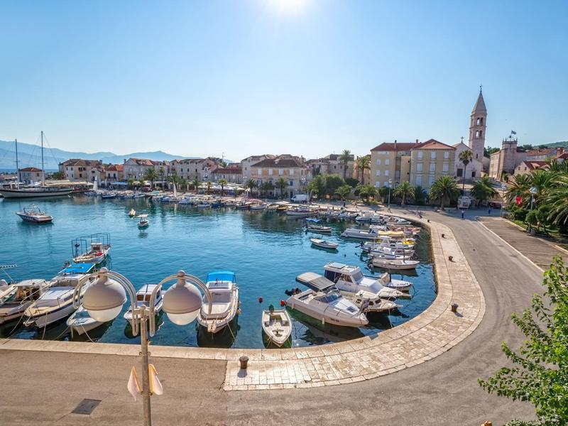 Zonnige havenpromenade met boten en historische gebouwen waaronder een kerktoren.