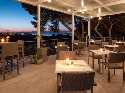 Terrasse confortable avec tables dressées et vue sur le coucher du soleil en bord de mer.