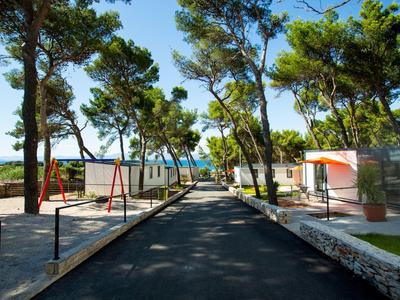 Route asphaltée entre des maisons de vacances et des arbres avec vue sur la mer en arrière-plan