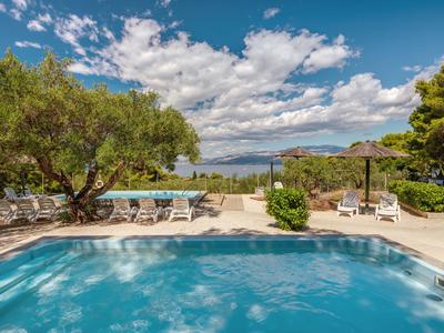 Espace piscine avec chaises longues, arbres et vue sur la mer sous un ciel nuageux.