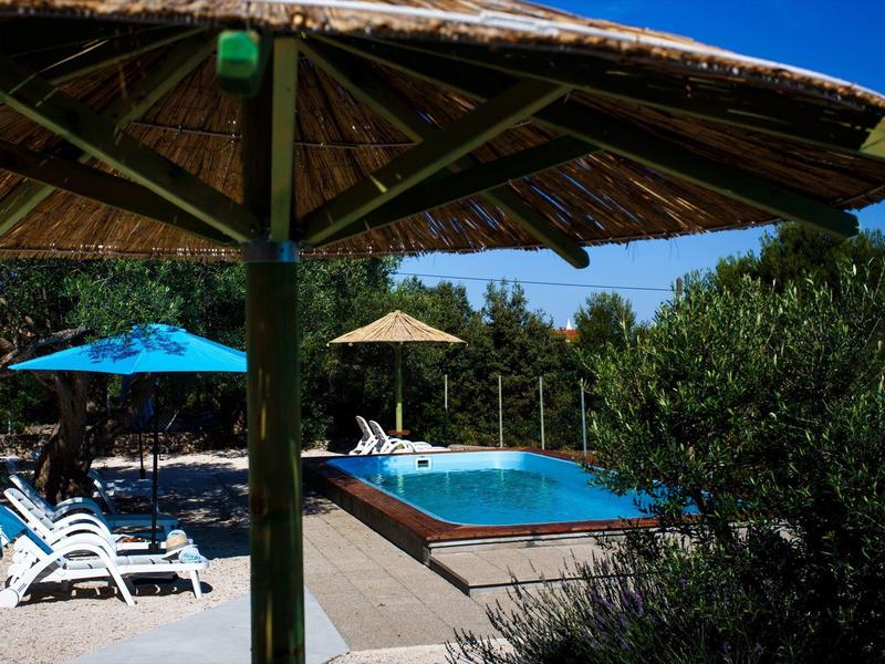 Espace piscine avec chaises longues, parasols et beaucoup de verdure dans un jardin d'hôtel.