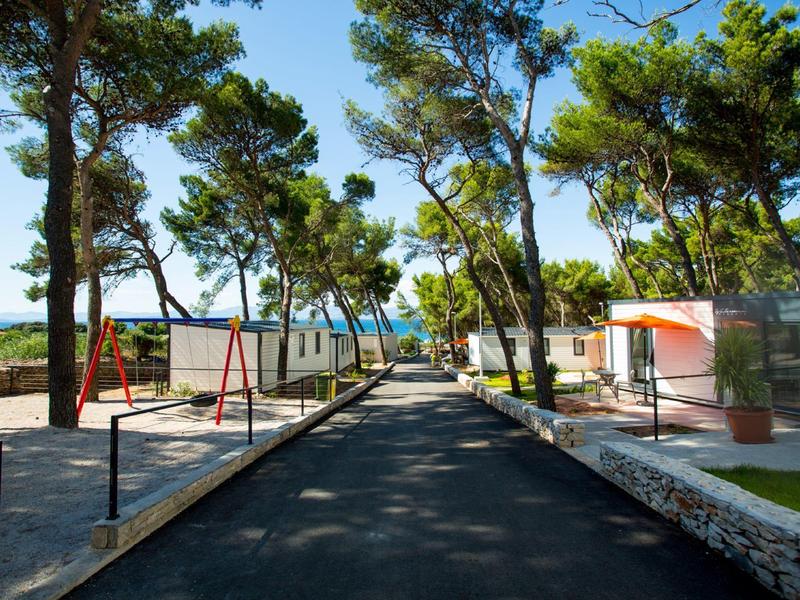 Route asphaltée entre des maisons de vacances et des arbres avec vue sur la mer en arrière-plan