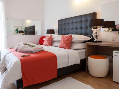 Camera d'hotel moderna con letto matrimoniale, accenti rossi e toeletta con sgabello.