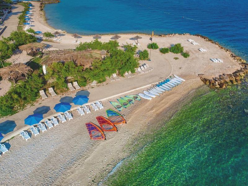 Spiaggia con lettini, ombrelloni e acqua turchese limpida lungo la costa.