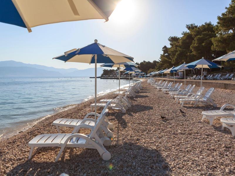 Spiaggia con ombrelloni e lettini lungo il mare calmo con cielo sereno.