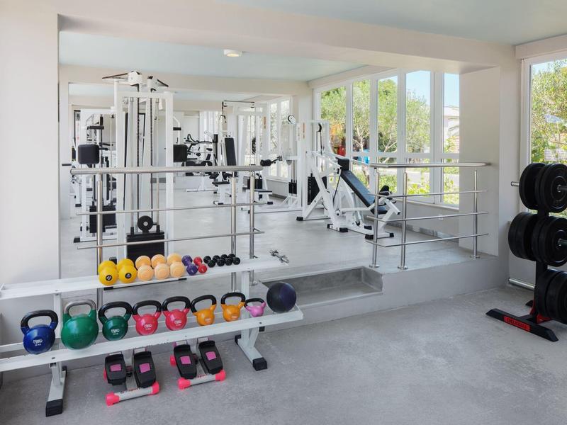 Palestra luminosa con pesi, manubri e attrezzi per il fitness vicino a grandi finestre.