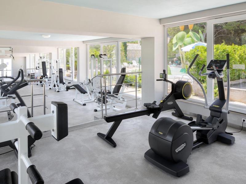 Sala fitness luminosa con attrezzature moderne e grandi finestre con vista sul giardino.