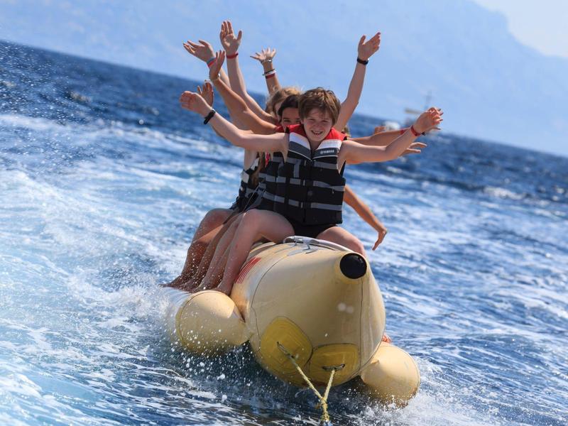Gruppo che si diverte su una banana trainata in mare con giubbotti di salvataggio.