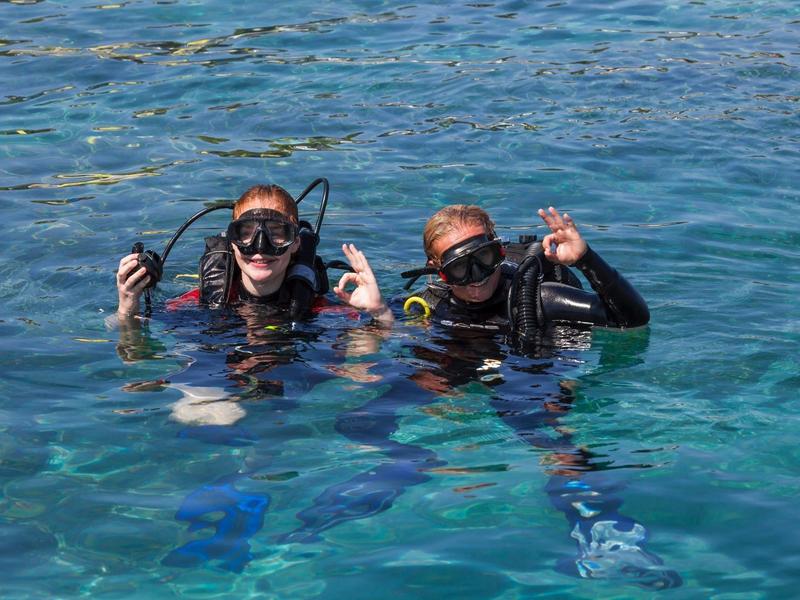 Due subacquei nell'acqua con maschere e attrezzatura fanno gesti.