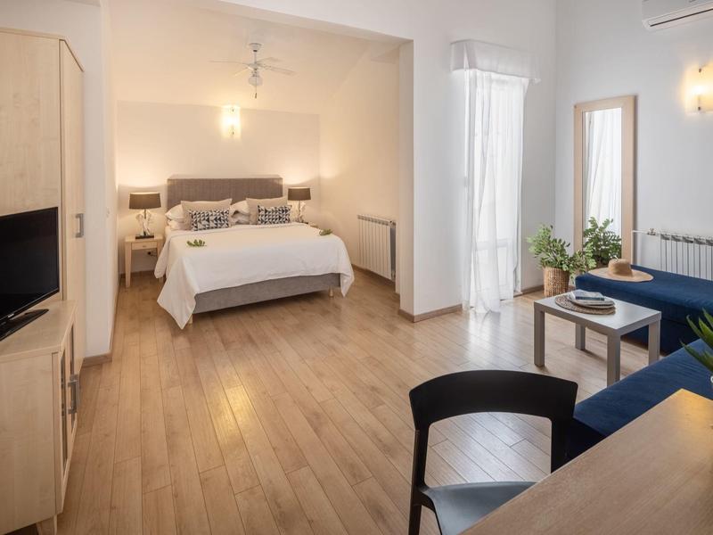 Camera d'hotel luminosa con letto matrimoniale, pavimento in legno e arredamento moderno.