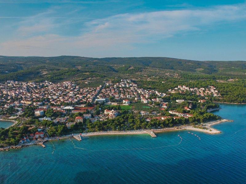 Città costiera con spiagge, case e colline verdi sotto un cielo azzurro.