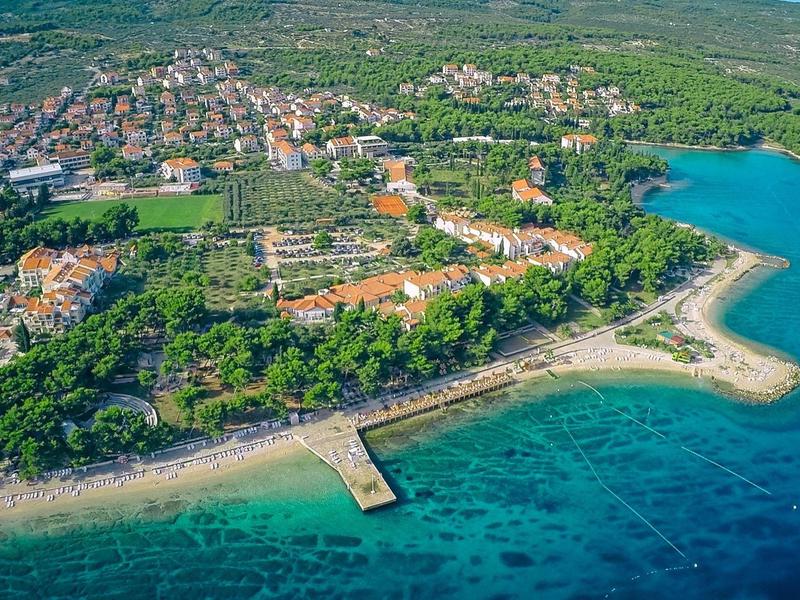 Veduta aerea di una città costiera con spiaggia, molo e acqua limpida blu.