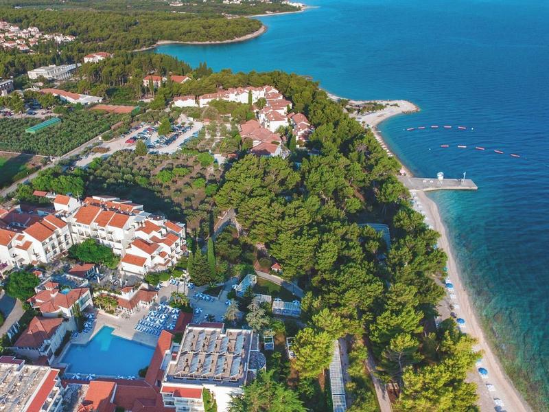 Veduta aerea di una località balneare con foresta verde e mare turchese.