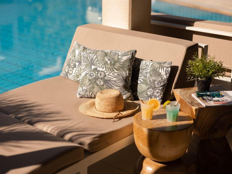 Area relax con cuscini, cappello di paglia e bevande accanto a una piscina.