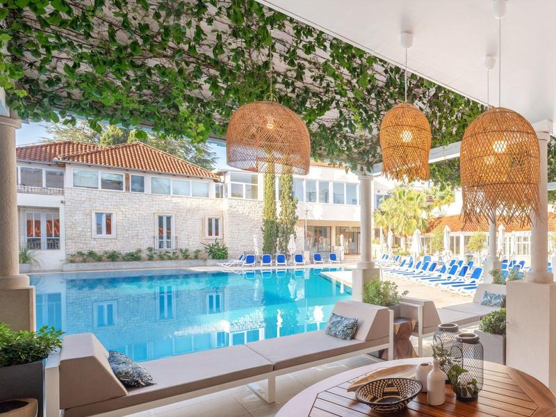 Vista sulla piscina con sedie e lampade sotto una copertura verde.