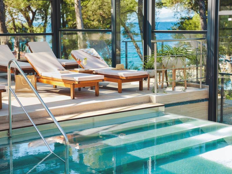 Area piscina di lusso con lettini e parete in vetro con vista mare.