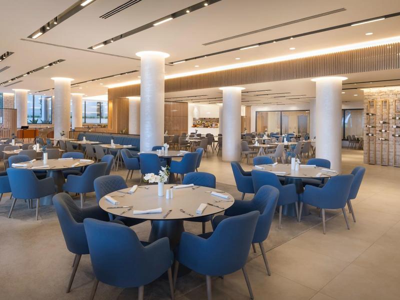 Moderner Gastraum mit blauen Stühlen, runden Tischen und heller, eleganter Beleuchtung.