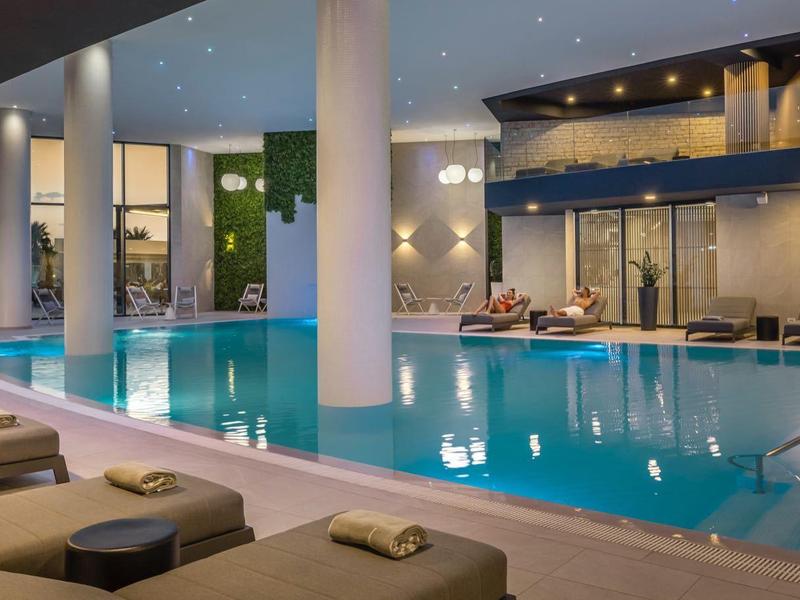 Moderner Innenpool mit blauen Fliesen, Liegestühlen und warmem Licht in elegantem Raum.