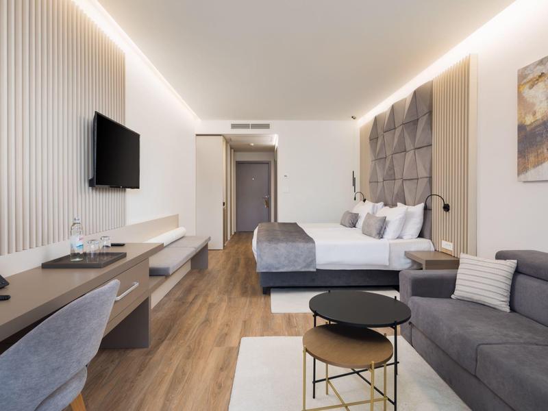 Modern eingerichtetes Hotelzimmer mit Doppelbett, Sofa, Schreibtisch und Holzfußboden.