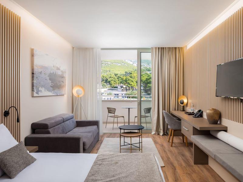 Modern eingerichtetes Hotelzimmer mit Bett, Sofa, Schreibtisch und Balkon mit Blick ins Grüne.