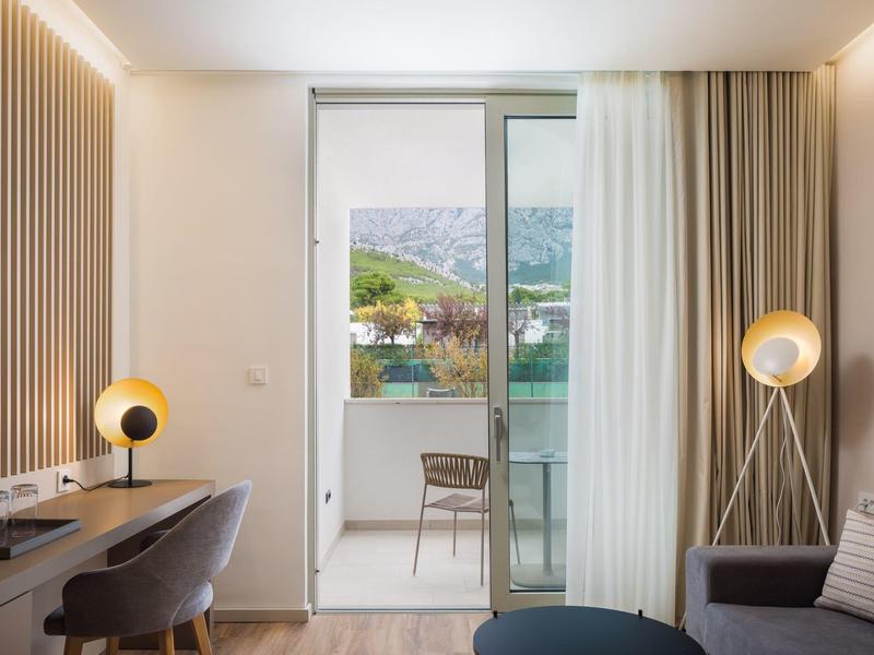 Helles Wohnzimmer mit Schreibtisch, Stühlen, Stehlampe und Balkon mit Bergblick.