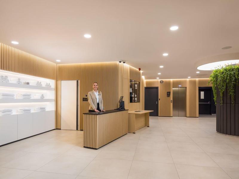 Heller, moderner Empfangsbereich mit Holzdetails, Pflanze in großem Topf und minimalistischer Theke.